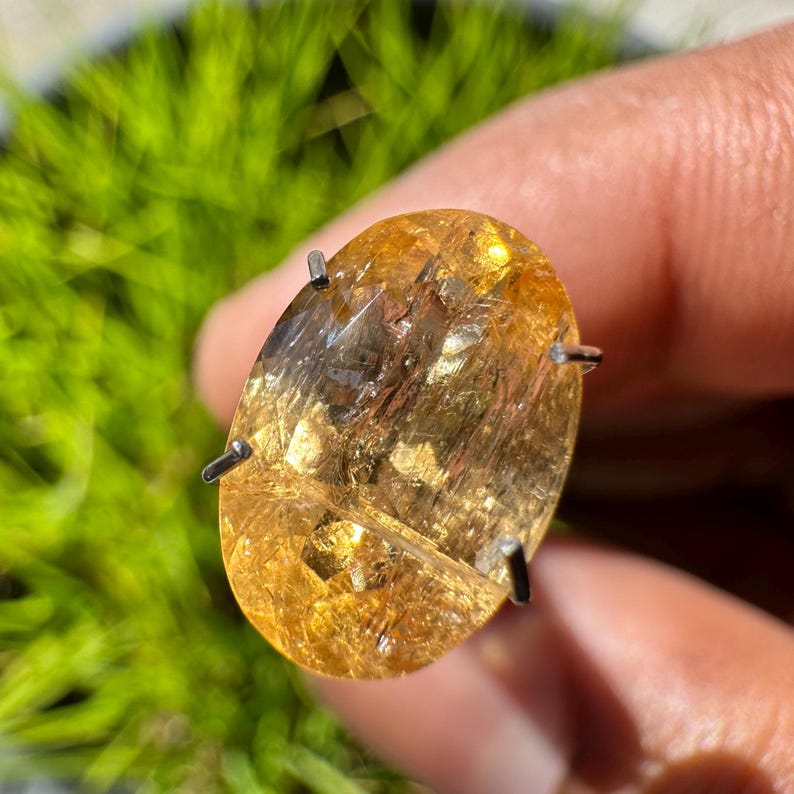 May include: A large, oval-shaped, golden citrine gemstone with a clear, glassy finish. The stone is set in a prong setting with four prongs.