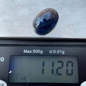 May include: A dark blue oval gemstone weighing 1.120 carats on a digital scale.