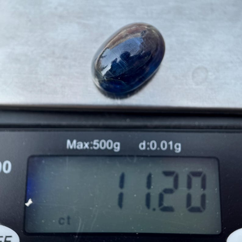 May include: A dark blue oval gemstone weighing 1.120 carats on a digital scale.