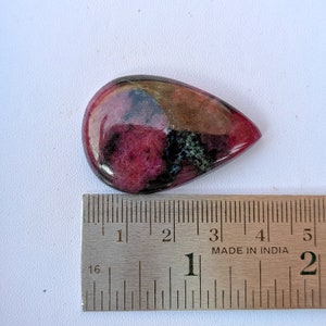 Puede incluir: Una piedra preciosa en cabuj&oacute;n en forma de l&aacute;grima con un patr&oacute;n rosa, verde y negro. La piedra mide aproximadamente 2,5 cm de largo y se mide con una regla.