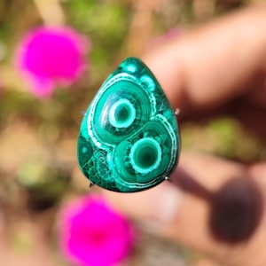 May include: A green and white malachite cabochon with a swirling pattern. The cabochon is set in a silver bezel and is ready to be made into jewelry.