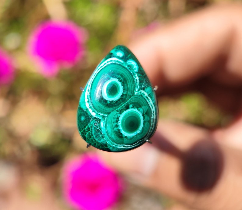 May include: A green and white malachite cabochon with a swirling pattern. The cabochon is set in a silver bezel and is ready to be made into jewelry.