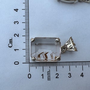 K&ouml;nnte beinhalten: Ein klarer Quarz-Anh&auml;nger mit braunen Einschl&uuml;ssen, gefasst in einer silbernen Fassung und an einer silbernen &Ouml;se befestigt. Der Anh&auml;nger ist etwa 2 cm lang.