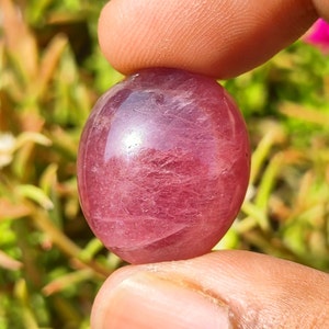 Può includere: Una pietra preziosa rosa liscia di forma ovale con un aspetto traslucido. La pietra preziosa presenta un motivo sottile e vorticoso su tutta la superficie.