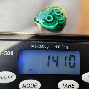 May include: A green and white malachite cabochon gemstone weighing 14.10 carats. The gemstone is teardrop shaped and has a swirling pattern.
