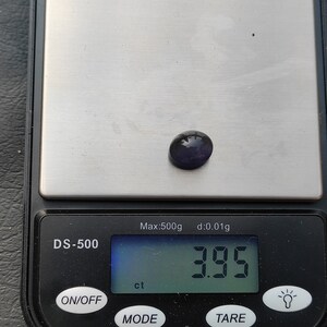 May include: A digital scale with a purple gemstone on the weighing platform. The scale reads "3.95 ct" and has the text "DS-500", "Max:500g", "d:0.01g", "ON/OFF", "MODE", and "TARE" on the display.