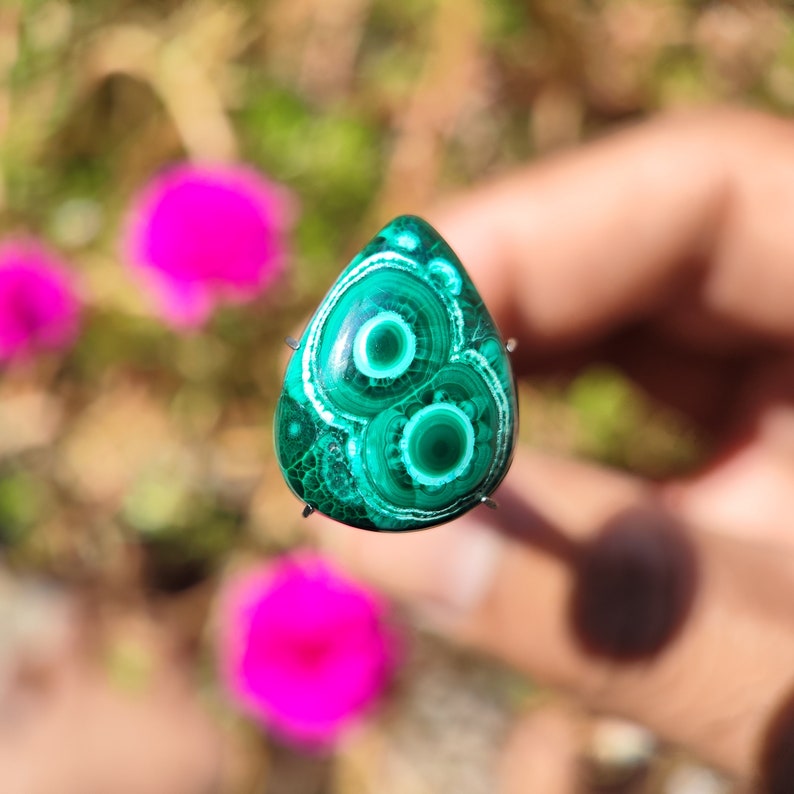 May include: A green and white malachite cabochon with a swirling pattern. The cabochon is set in a silver bezel and is ready to be made into jewelry.
