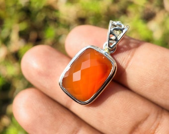 May include: A silver pendant with an orange carnelian gemstone. The pendant has a detailed filigree design and is set in a rectangular shape.