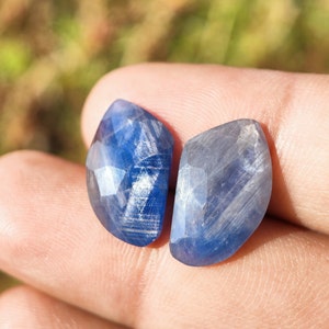 Peut inclure: Deux pierres précieuses de saphir bleu avec une taille facetée et un motif strié. Les pierres précieuses sont tenues dans une main.