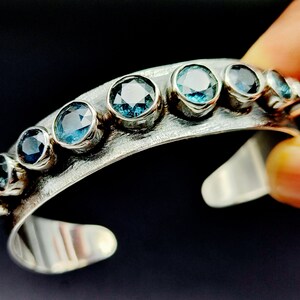 Può includere: Un braccialetto rigido in argento con finitura martellata e una fila di pietre preziose blu.