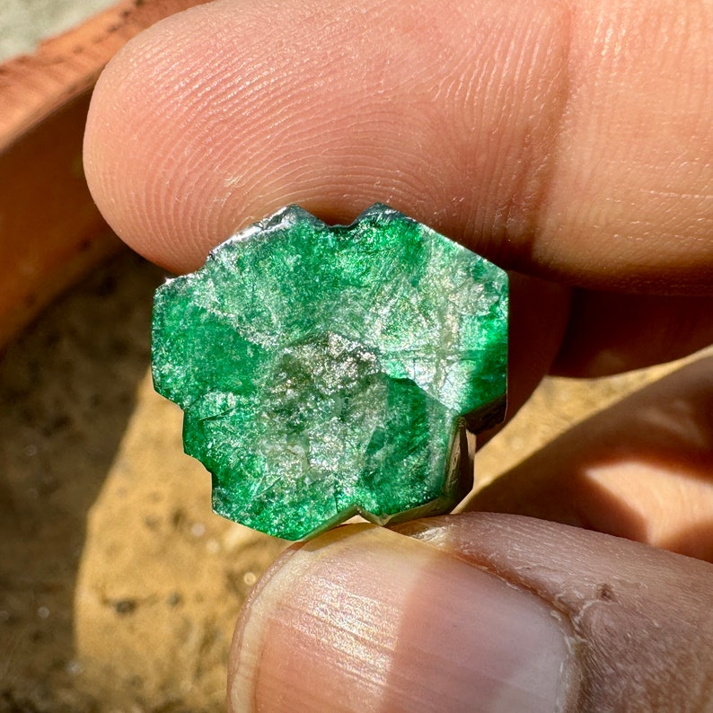 May include: A large, faceted, green emerald gemstone with a rough, natural finish.