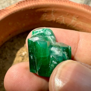 May include: A large, faceted, green emerald gemstone with white inclusions. The emerald is held in a hand.
