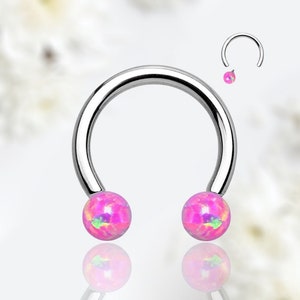 Puede incluir: Un anillo de plata en forma de herradura con dos bolas de ópalo rosa en los extremos. El anillo está sobre un fondo blanco.