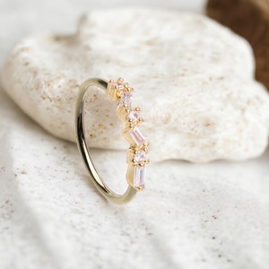 May include: A gold ring with a row of clear, baguette-shaped stones set in a delicate, curved design.