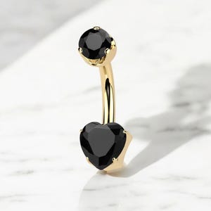 May include: Gold belly button ring with a black heart-shaped gem and a smaller black round gem at the top.
