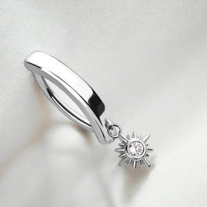 Puede incluir: Un aro de plata para la oreja con un pequeño encanto de estrella colgante. La estrella tiene un solo cristal transparente en el centro.