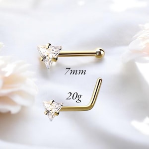Può includere: Due piercing al naso color oro con gemme triangolari trasparenti. Uno è dritto, l'altro a forma di L. Il testo indica che quello dritto è lungo 7 mm. Il piercing a L è di 20 g. Su sfondo bianco.