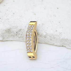 May include: A gold-toned nose ring with a curved design and two rows of clear cubic zirconia stones.