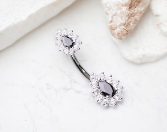 Pode incluir: Um piercing de umbigo prateado com duas pedras pretas em forma de lágrima cercadas por strass transparentes.