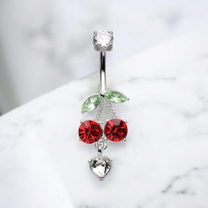 May include: Silver belly button ring with a dangling cherry charm. The charm features two red crystal cherries with green crystal leaves and a small heart-shaped crystal.