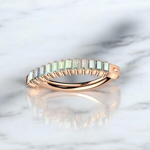 Op de afbeelding: Ros&eacute;gouden ring met een rij rechthoekige, iriserende edelstenen. De edelstenen zijn dicht op elkaar geplaatst, waardoor een doorlopende band van kleur ontstaat. De ringband heeft een gladde, gepolijste afwerking.