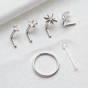 Puede incluir: Conjunto de joyas para la nariz, que incluye varios piercings en forma de L con piedras preciosas transparentes, un piercing en forma de estrella y un piercing en forma de media luna. También se incluye un aro para la nariz y un hueso nasal transparente. Todas las piezas son plateadas.