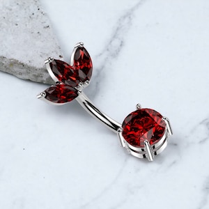 May include: A silver belly button ring with a red gemstone in the center and three smaller red gemstones on the top in a leaf design.