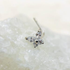 Pode incluir: Um piercing de nariz de prata com um design de flor de cristal transparente.