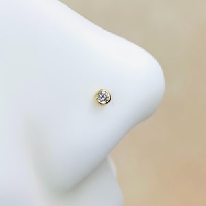 May include: A gold nose ring with a clear round gemstone.