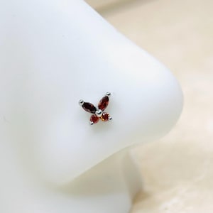 May include: A silver nose ring with a small butterfly design featuring red and orange gemstones.