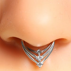 Puede incluir: Anillo de nariz de plata con un diseño de tres puntas y tres piedras de circonita cúbica transparentes.