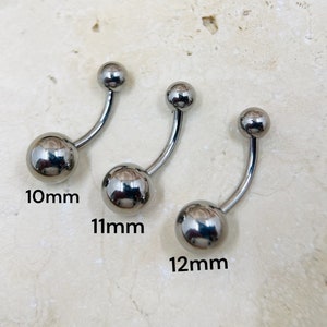 May include: Three silver-colored belly button rings. Each ring has a curved barbell design with a small ball on top and a larger ball at the bottom. The sizes are 10mm, 11mm, and 12mm.
