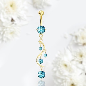 Puede incluir: Anillo de ombligo dorado con un colgante de cristal azul. El colgante tiene un diseño curvo con varios cristales azules más pequeños.