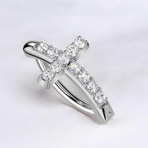 May include: A silver-colored cross-shaped earring with a row of clear, sparkling stones along each arm. The earring has a curved bar for insertion and is set against a white background.