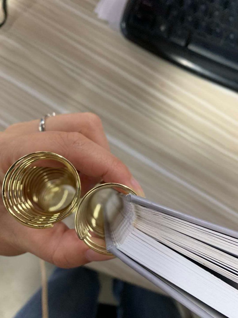 May include: Two gold metal binder rings holding a stack of white pages together.