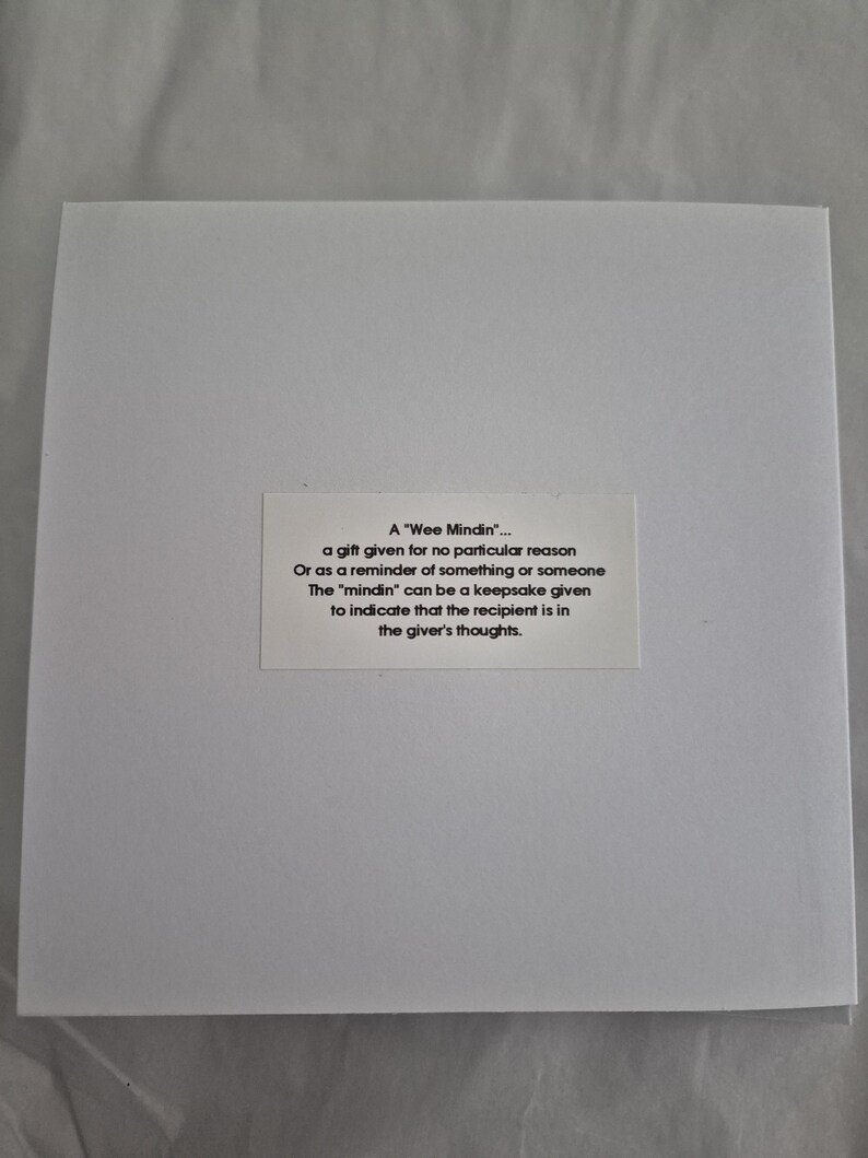 May include: A white card with black text explaining the meaning of a "Wee Mindin". A "Wee Mindin" is a gift given for no particular reason or as a reminder of something or someone. The "mindin" can be a keepsake given to indicate that the recipient is in the giver's thoughts.