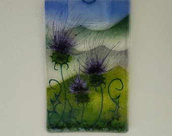 Könnte beinhalten: Ein Glaskunstwerk mit drei violetten Distelblumen mit grünen Stielen und Blättern vor einem blauen und grünen Hintergrund.
