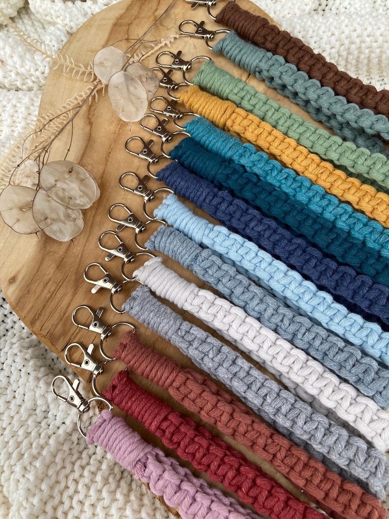 May include: A collection of colorful, braided keychains with silver key rings. The keychains are made of different colors of yarn, including red, orange, yellow, green, blue, purple, and brown.