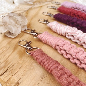 Op de afbeelding: Vijf handgemaakte macramé sleutelhangers in tinten van roze, rood en paars. De sleutelhangers zijn gemaakt met een dik, gevlochten koord en hebben zilveren sleutelringen.