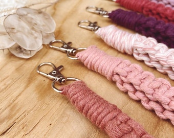May include: Five handmade macrame keyrings in shades of pink, red, and purple. The keyrings are made with a thick, braided cord and have silver key rings.