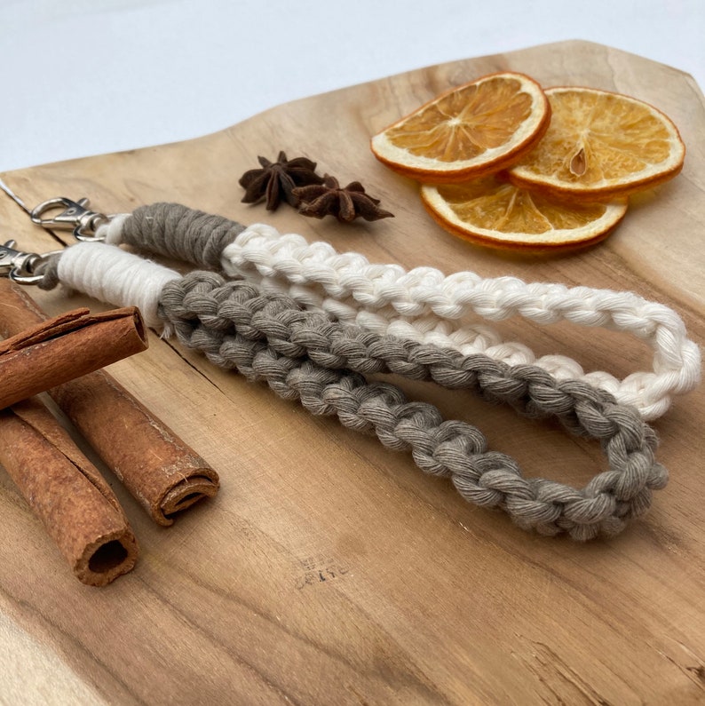 May include: A white and gray braided keychain with a silver key ring. The keychain is on a wooden surface with dried orange slices and cinnamon sticks.