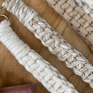 May include: Three handmade macrame keychains in beige, white, and cream colors. The keychains are made with a thick, braided rope and have a simple, minimalist design.