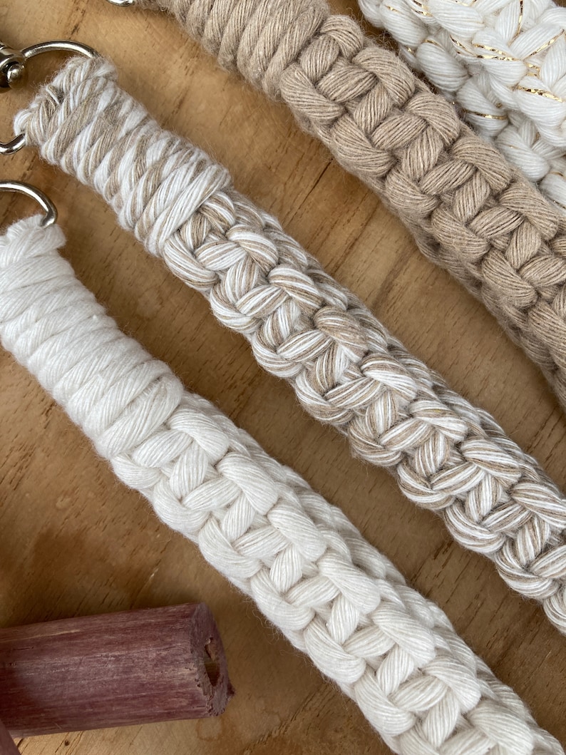 May include: Three handmade macrame keychains in beige, white, and cream colors. The keychains are made with a thick, braided rope and have a simple, minimalist design.