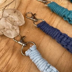 May include: Three keychains with different colored braided cords. The cords are light blue, dark blue, and teal. Each keychain has a silver metal ring and a silver metal hook.
