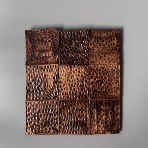 May include: A square grid of nine individual tiles arranged in a three-by-three pattern. Each tile features a dark, metallic copper finish with a distinct hammered, dimpled texture across the entire surface, creating a uniform, reflective appearance.