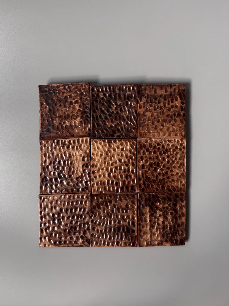 May include: A square grid of nine individual tiles arranged in a three-by-three pattern. Each tile features a dark, metallic copper finish with a distinct hammered, dimpled texture across the entire surface, creating a uniform, reflective appearance.