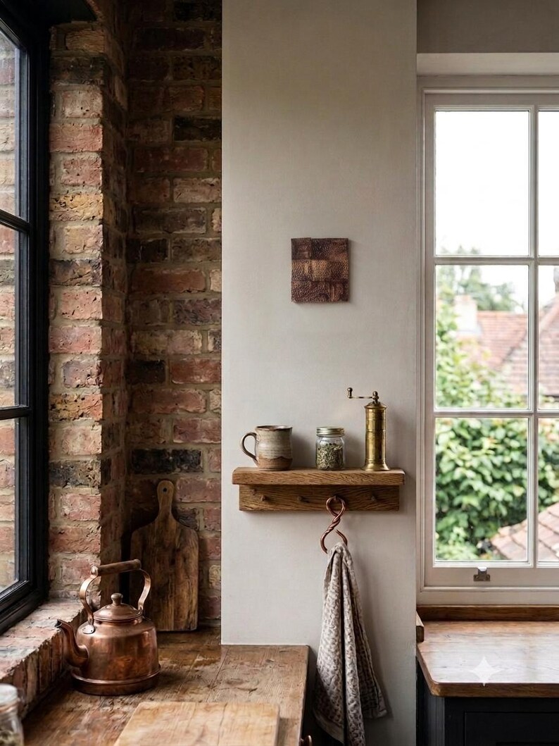 May include: A wooden wall shelf with three hooks, holding a ceramic mug, a glass jar, and a brass pepper mill. A textured brown square wall art piece hangs above the shelf, while a copper kettle and wooden cutting board sit nearby.