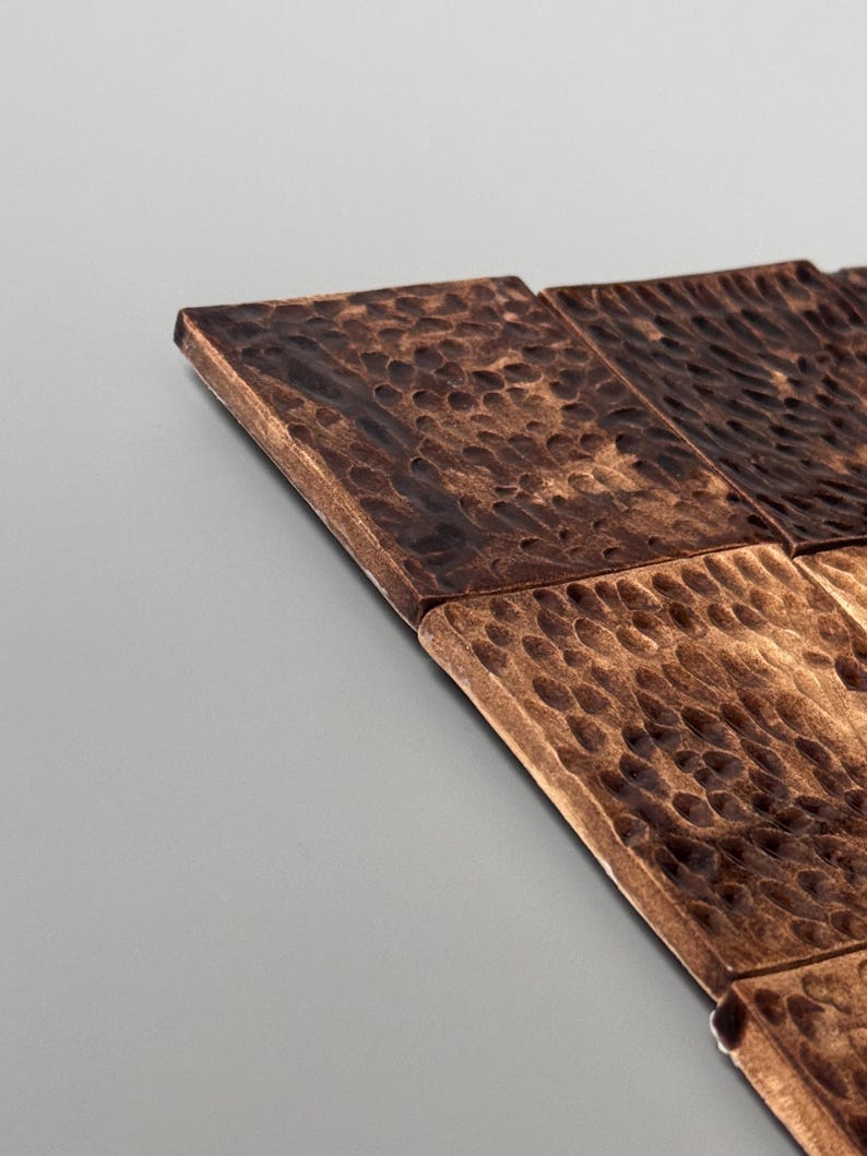 May include: A collection of square tiles featuring a dark brown, metallic finish with a hammered, dimpled texture across the surface. The tiles are arranged in a grid pattern, showcasing a reflective sheen and a rugged, uneven appearance.