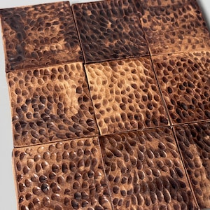 May include: A grid of nine square copper tiles arranged in a three-by-three pattern. Each tile features a distinct hammered texture with a dark, oxidized patina that highlights the indentations across the metallic, reddish-brown surface.