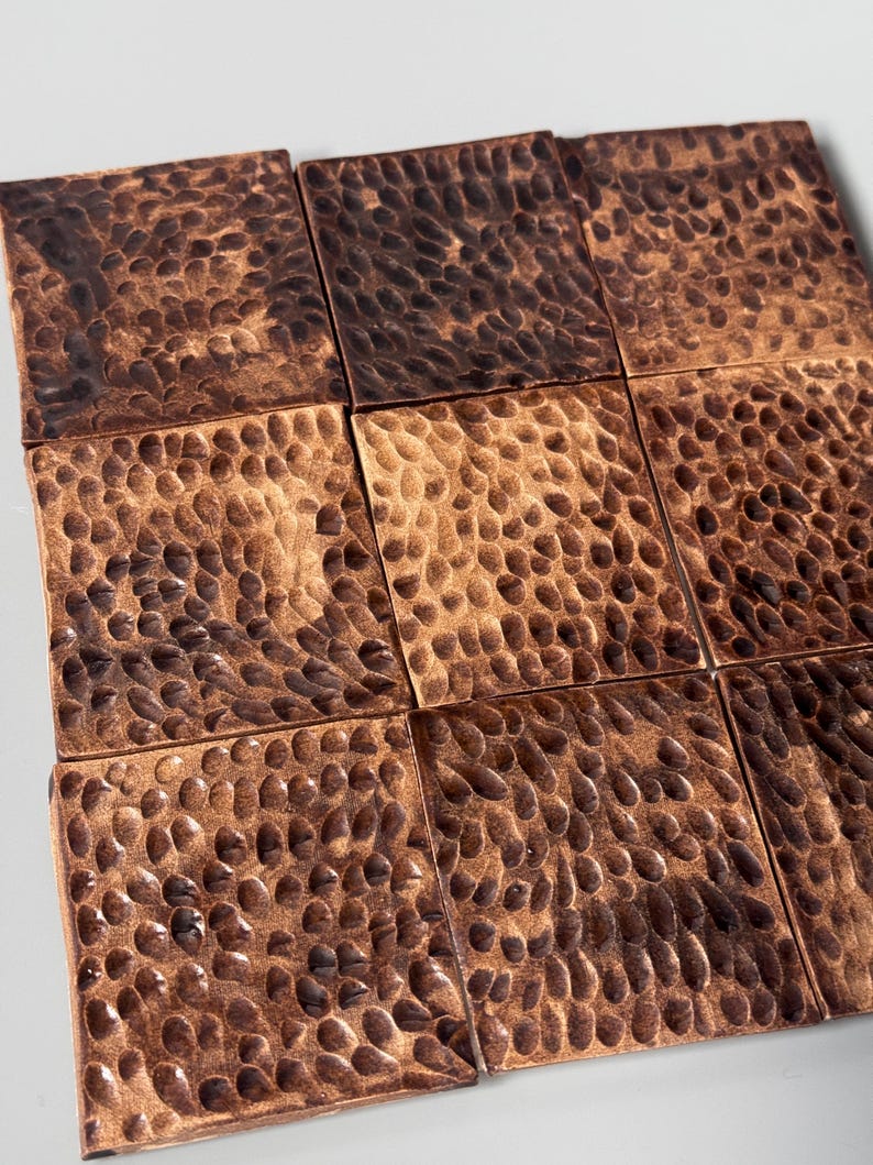 May include: A grid of nine square copper tiles arranged in a three-by-three pattern. Each tile features a distinct hammered texture with a dark, oxidized patina that highlights the indentations across the metallic, reddish-brown surface.